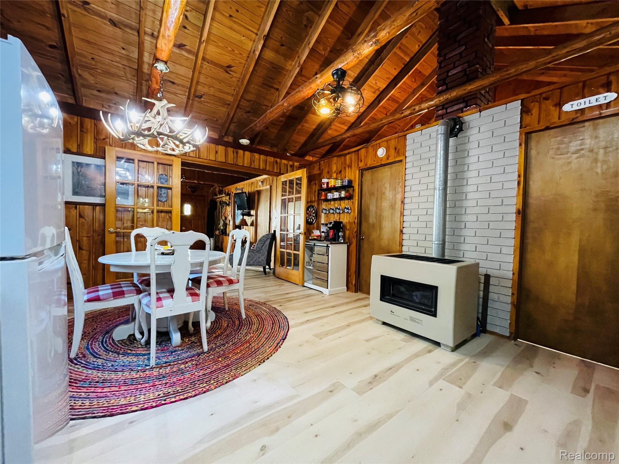 417 Ogemaw Road Rose City, MI 48654 - Photo 9 of 26 Wood-paneled walls and ceiling with exposed beams, light wood-finish flooring, and a built-in stove with a white brick surround