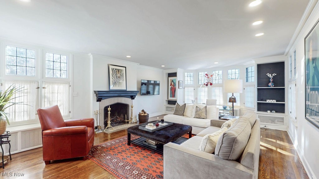 Living room featuring hardwood floors, leaded glass windows, built-ins, bay window and stone fireplace.