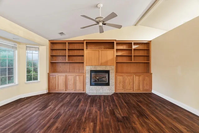 an empty room with wooden floor a fireplace a ceiling fan and windows