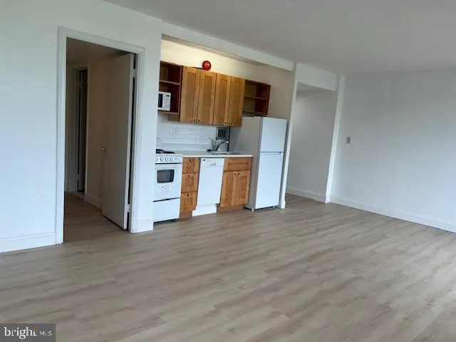a view of kitchen and empty room with wooden floor