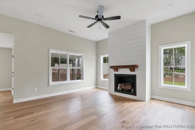 a view of an empty room with wooden floor fireplace and a window