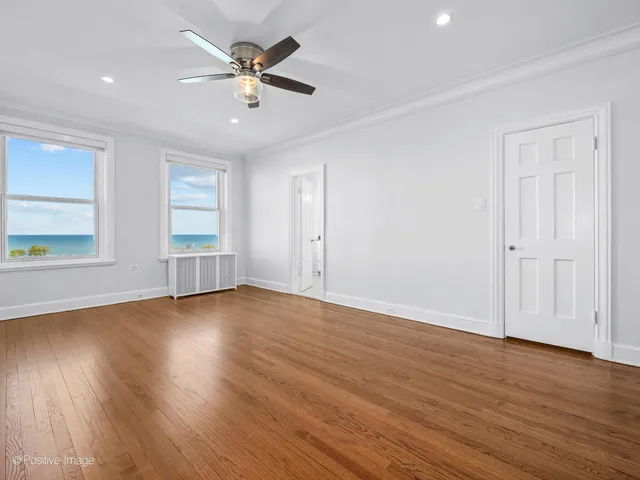 an empty room with wooden floor chandelier fan and windows