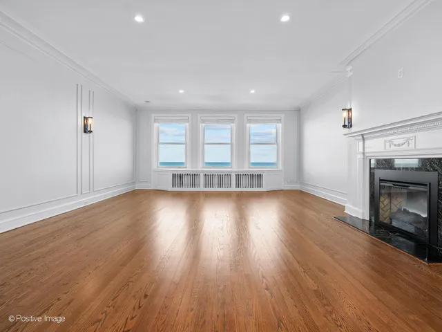 an empty room with wooden floor fire place and windows