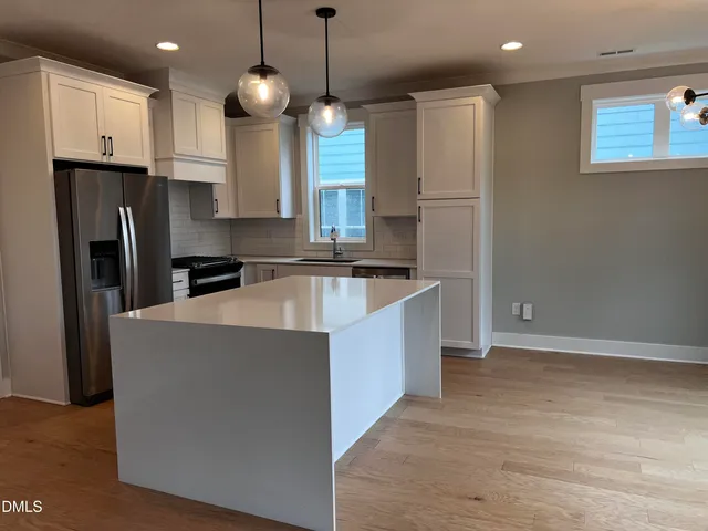 a kitchen with stainless steel appliances granite countertop a refrigerator a oven a sink and white cabinets with wooden floor