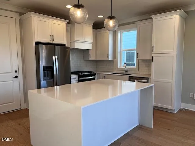 a kitchen with stainless steel appliances granite countertop a sink a stove a refrigerator and island with wooden floor