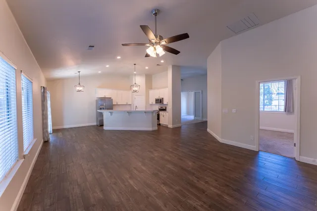 a view of an empty room with wooden floor and a ceiling fan