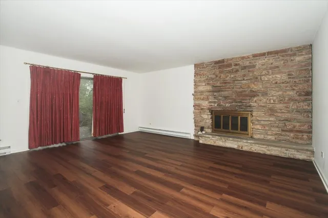 a view of an empty room with wooden floor and a fireplace