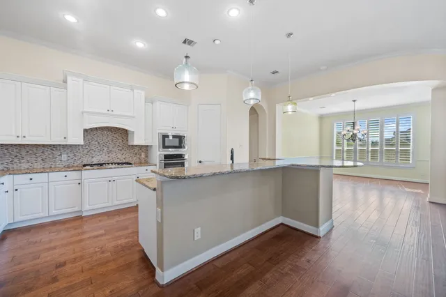 a kitchen with stainless steel appliances granite countertop a stove a sink and white cabinets with wooden floor
