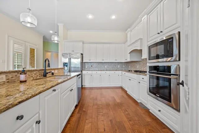 a large kitchen with granite countertop a stove top oven a sink dishwasher and white cabinets with wooden floor
