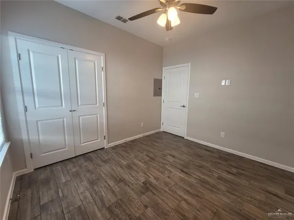 an empty room with wooden floor fan and windows