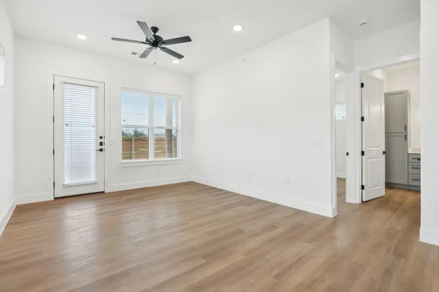 a view of an empty room with wooden floor and a ceiling fan