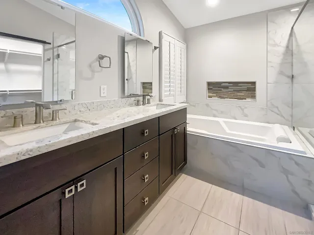 a bathroom with a granite countertop double vanity sink a mirror and a bathtub