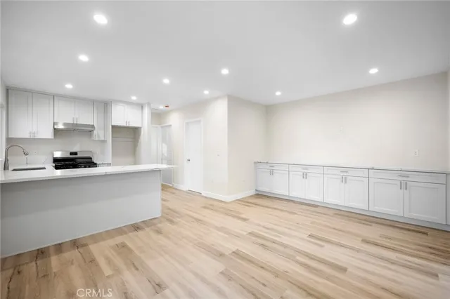 a view of kitchen with kitchen island granite countertop a stove top oven a sink and white cabinets with wooden floor