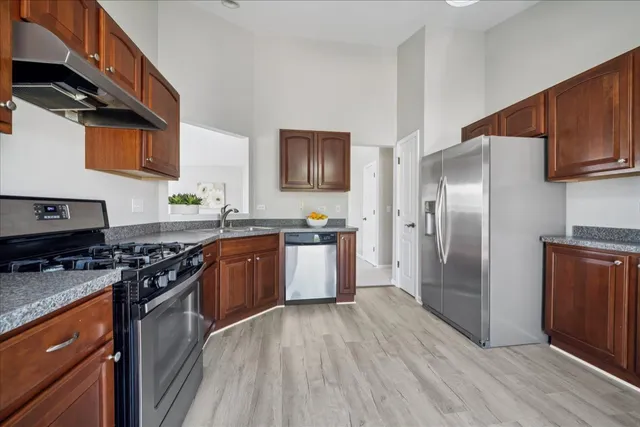 a kitchen with stainless steel appliances granite countertop a stove a refrigerator a sink dishwasher and wooden cabinets with wooden floor