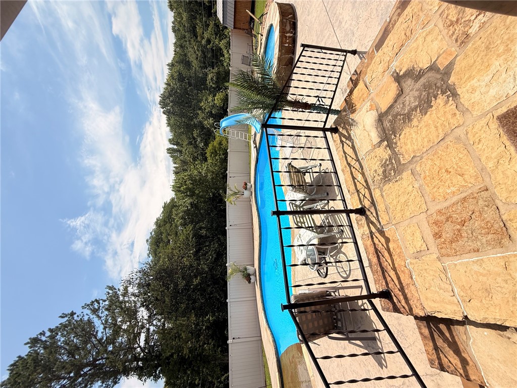 1224 River Road Pottsville, AR 72858 - Photo 20 of 37 Expansive backyard featuring a blue-tiled swimming pool with a slide, an elevated circular spa, and a flagstone patio with wrought iron railings