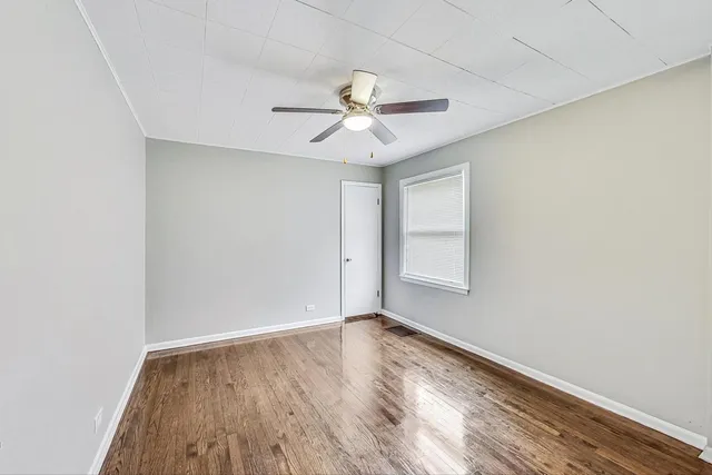 an empty room with wooden floor ceiling fan and windows
