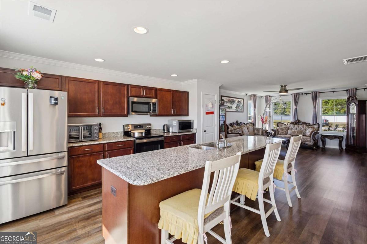 455 Tondee Way Midway, GA 31320 - Photo 11 of 52 a kitchen with stainless steel appliances granite countertop a refrigerator a stove top oven a sink dishwasher a dining table and chairs with wooden floor