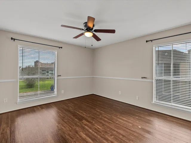 an empty room with wooden floor ceiling fan and windows
