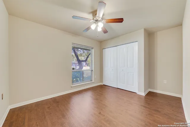 an empty room with wooden floor chandelier fan and windows