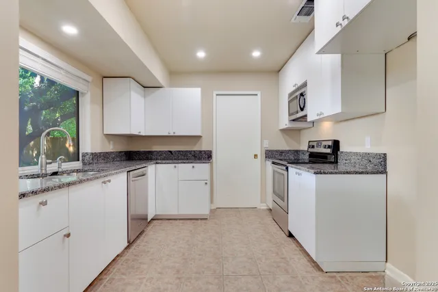 a kitchen with granite countertop white cabinets sink and stainless steel appliances