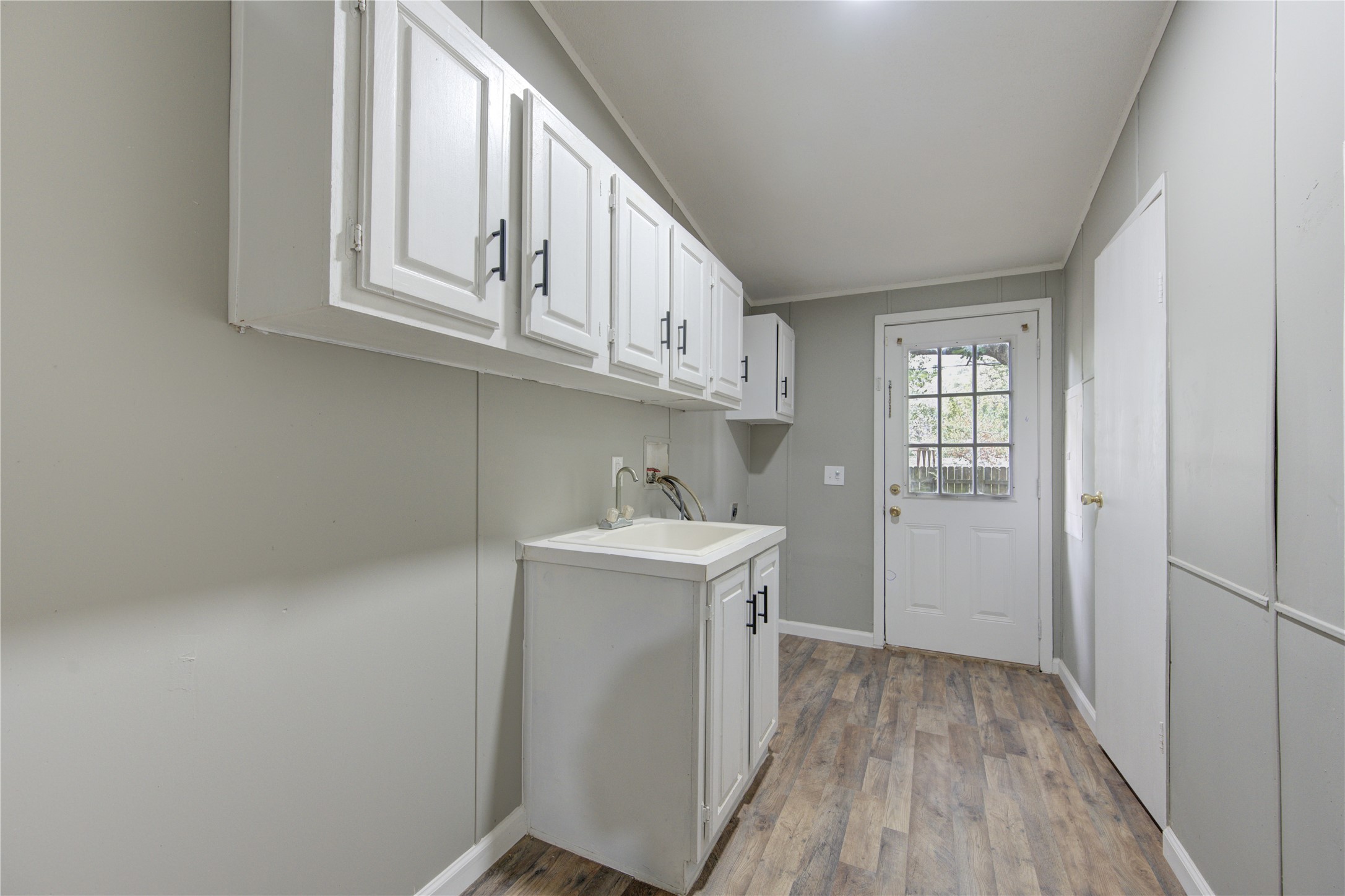 30226 Davis Street Magnolia, TX 77355 - Photo 26 of 50 Bright utility room with modern cabinetry, a sink, and wood-style flooring. Features a glass-paneled door leading outside, offering natural light and a pleasant view.