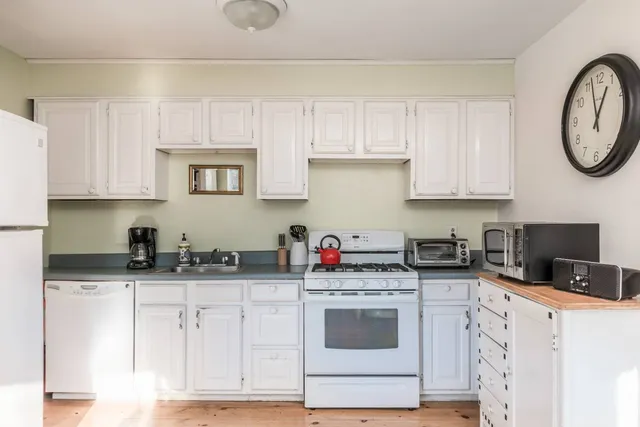 a kitchen with stainless steel appliances granite countertop a stove a sink dishwasher and white cabinets with wooden floor