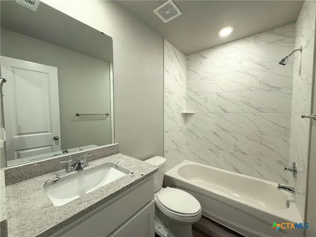 a bathroom with a granite countertop bathtub shower sink mirror vanity and toilet