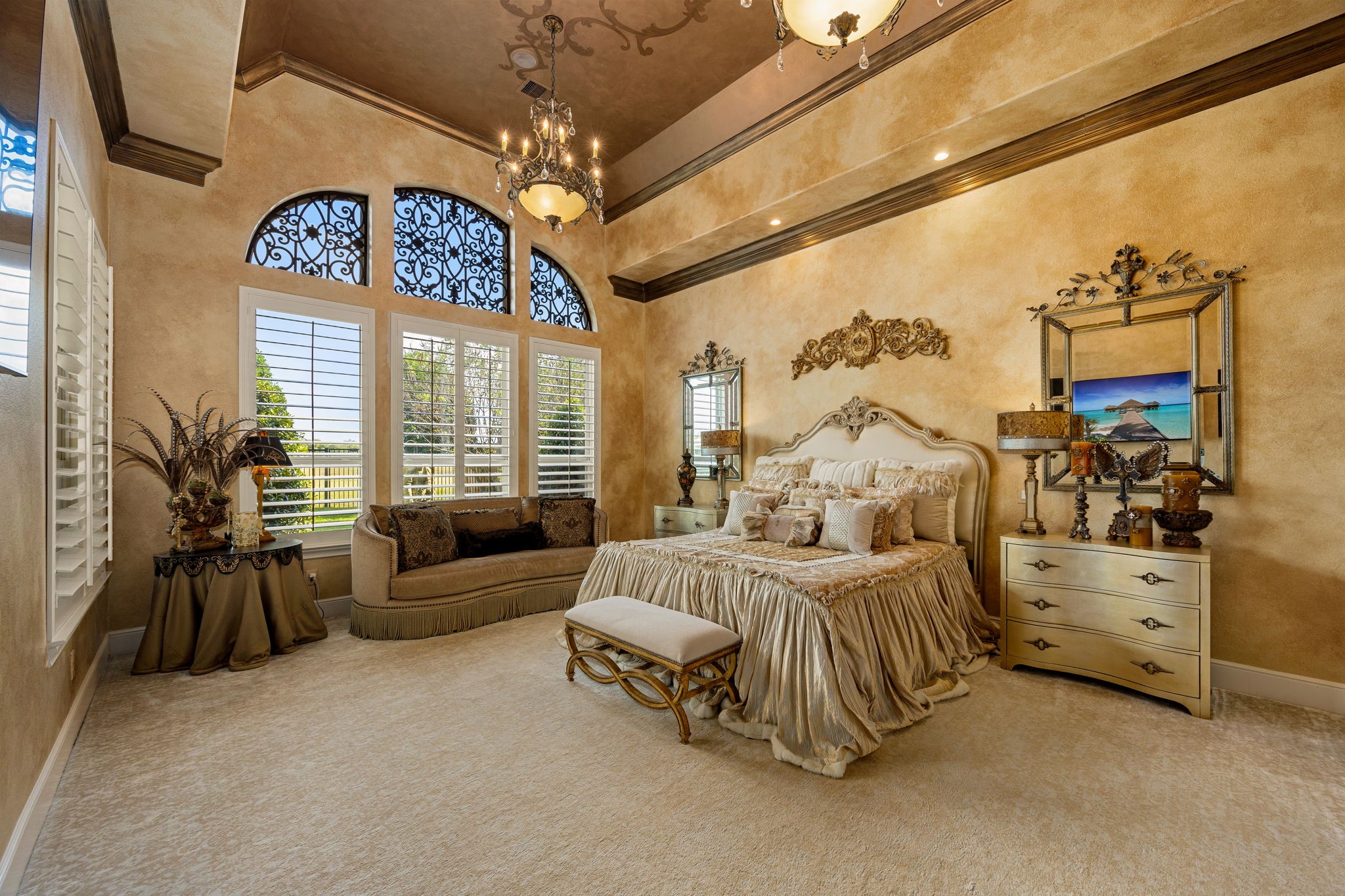 26515 Ashley Ridge Lane Katy, TX 77494 - Photo 24 of 50 Luxurious primary suite featuring large windows with elegant plantation shutters and wrought iron accents. Custom ceiling mural and dual chandeliers add a touch of sophistication, while the beveled ceiling design enhances the room’s spacious, architectural charm.