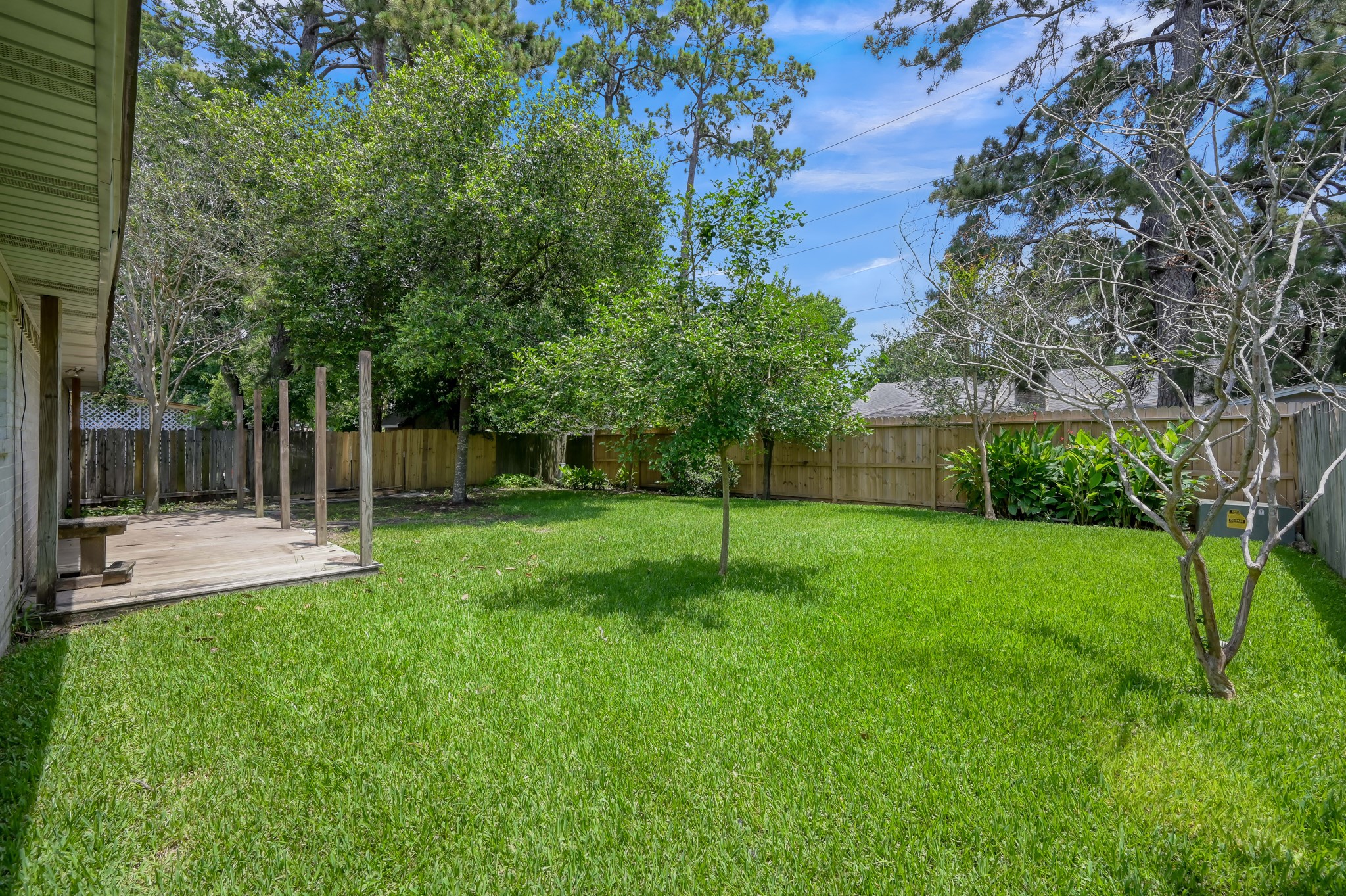 4314 Enchantedgate Drive Spring, TX 77373 - Photo 37 of 47 Spacious, fenced backyard with lush green grass and mature trees, providing a private and serene outdoor space. A small deck extends from the house, ideal for relaxing or entertaining.