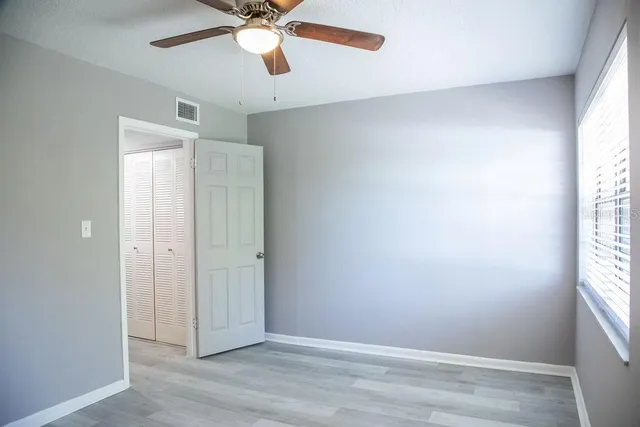 an empty room with wooden floor fan and windows