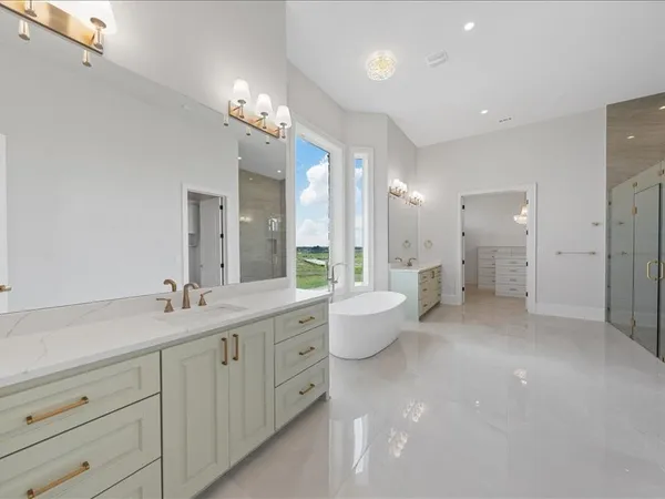 a spacious bathroom with a granite countertop tub double vanity sink a mirror a lamp a window and a bathtub