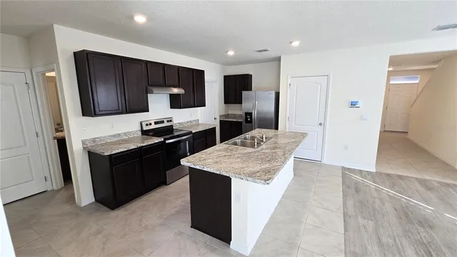 a kitchen with stainless steel appliances kitchen island granite countertop a refrigerator a stove and a sink with wooden cabinets