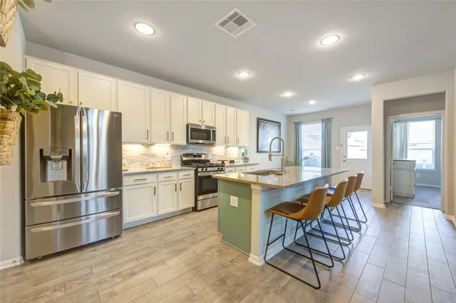 a kitchen with stainless steel appliances granite countertop a refrigerator a sink dishwasher a stove and white cabinets with wooden floor