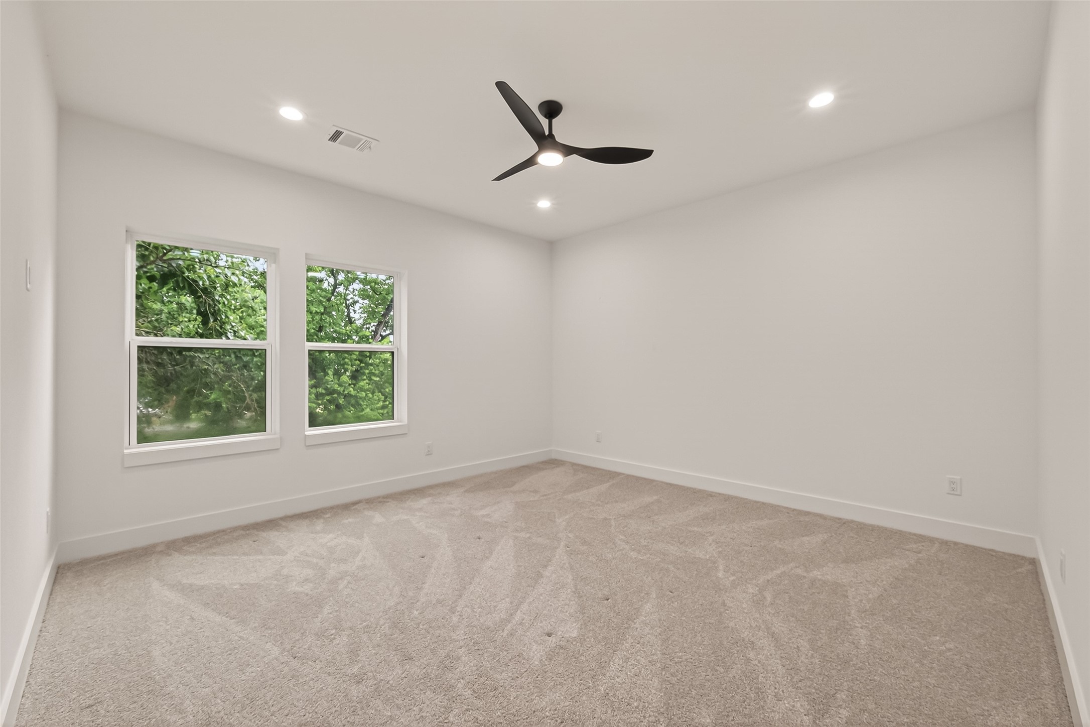 6808 Madrid Street Houston, TX 77021 - Photo 24 of 31 This room features clean white walls, a modern ceiling fan, and plush carpeting. Natural light streams through two large windows, offering a view of lush greenery, creating a bright and inviting space.