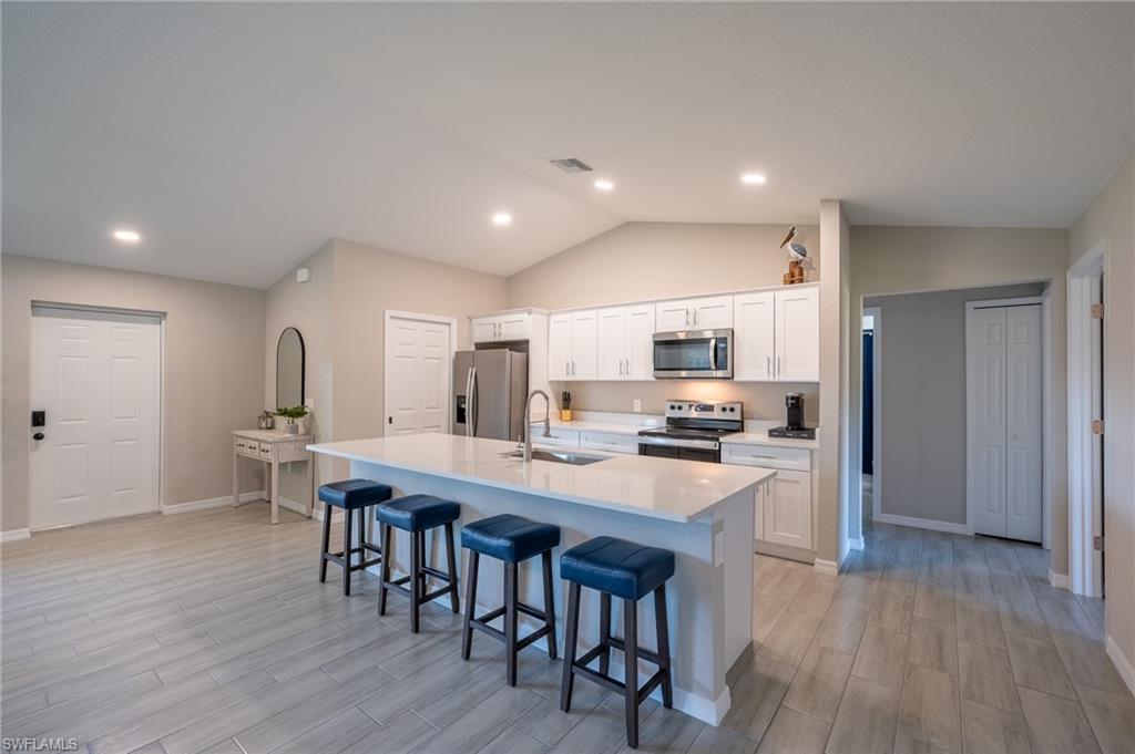8152 Pelican Road Fort Myers, FL 33967 - Photo 9 of 24 Modern kitchen featuring white cabinetry, stainless steel appliances, a white island with an integrated sink, and wood-finish flooring