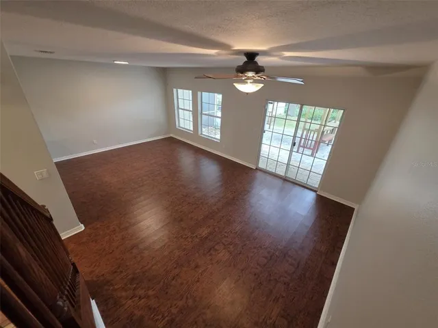 an empty room with wooden floor fan and windows