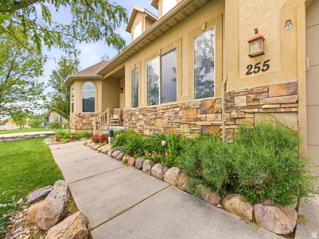 255 East 1200 North Mapleton, UT 84664 - Photo 2 of 37 Stucco exterior with stone veneer accents, concrete pathway, established landscaping with natural rock borders, and a covered porch with an arched window
