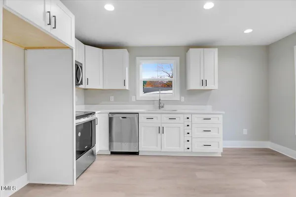 a view of an empty room with a window and kitchen view