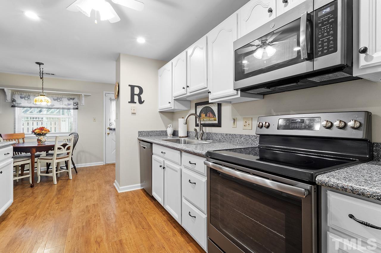 6921 Chamonix Place Raleigh, NC 27613 - Photo 3 of 30 a kitchen with stainless steel appliances granite countertop a stove top oven a sink dishwasher a dining table and chairs with wooden floor