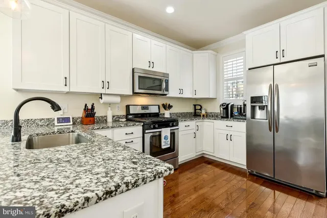 a kitchen with stainless steel appliances granite countertop a stove a sink a refrigerator and white cabinets