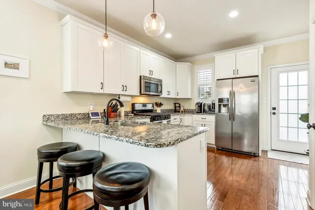 a kitchen with stainless steel appliances granite countertop a sink a stove a refrigerator cabinets and a dining table with wooden floor