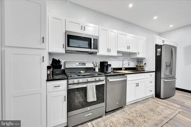 a kitchen with stainless steel appliances granite countertop white cabinets a sink a stove a refrigerator and white cabinets