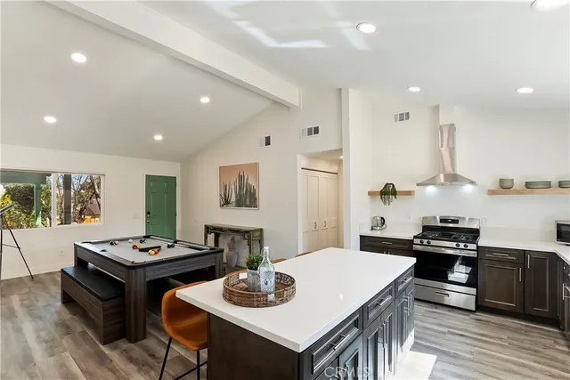 a kitchen with stainless steel appliances kitchen island granite countertop a stove a refrigerator a sink a dining table and chairs with wooden floor