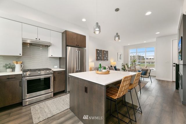 a kitchen with stainless steel appliances a stove a sink a refrigerator white cabinets and wooden floor