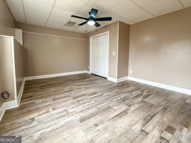an empty room with wooden floor ceiling fan and windows