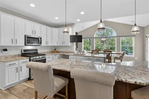 a open kitchen with stainless steel appliances granite countertop a stove a refrigerator a kitchen island a dining table and chairs