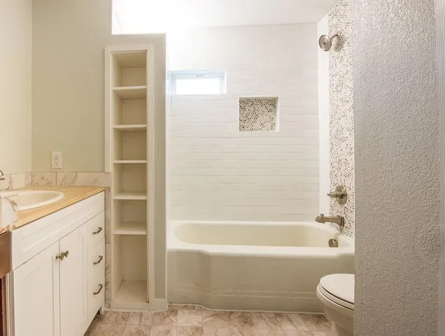 a bathroom with a granite countertop bathtub shower sink vanity and toilet