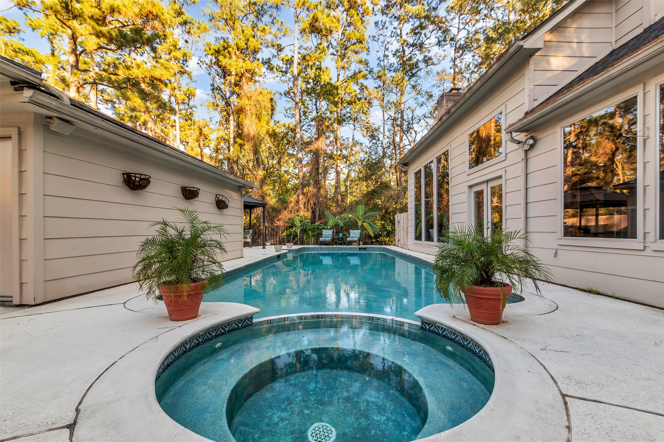 24102 Northcrest Drive Spring, TX 77389 - Photo 28 of 31 This inviting backyard features a sparkling pool and spa, surrounded by lush greenery and tall trees. The modern architecture of the home includes large windows offering plenty of natural light and a seamless indoor-outdoor transition. Perfect for relaxation and entertaining.
