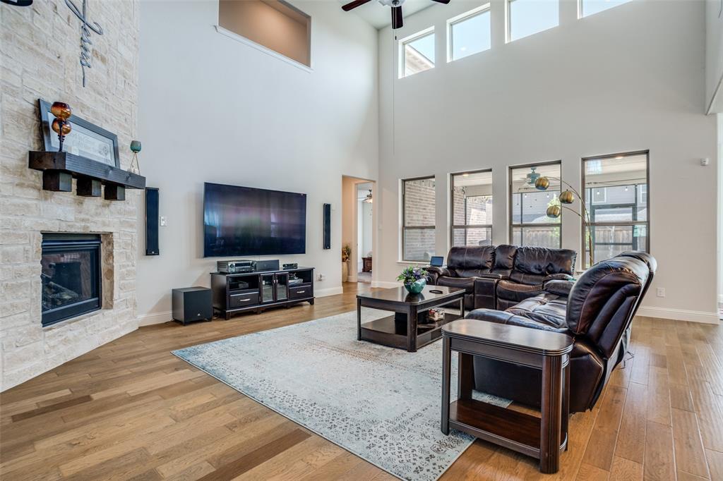 16380 Radstock Road Frisco, TX 75033 - Photo 2 of 39 Living area featuring a ceiling fan, light wood-style flooring, a stone fireplace, and a high ceiling
