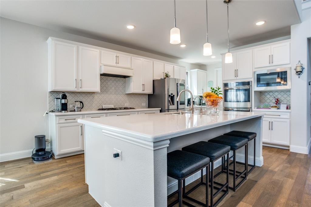 16380 Radstock Road Frisco, TX 75033 - Photo 7 of 39 Kitchen featuring a kitchen breakfast bar, a kitchen island with sink, stainless steel appliances, decorative light fixtures, and dark wood-style floors